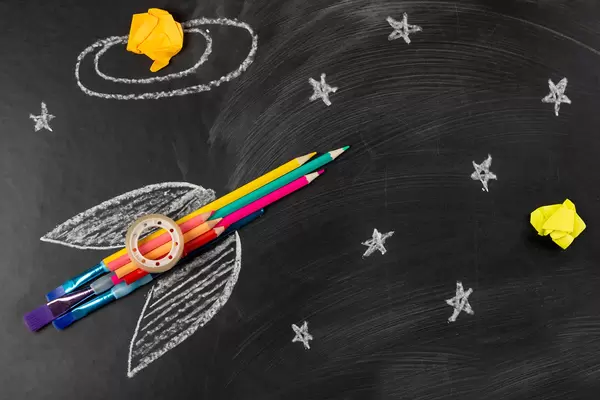 Spaceship or rocket made of school supplies on a dark background with chalk drawn stars
