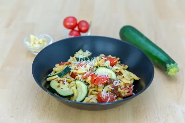 Spaetzle with dried tomatoes and zucchini with ingredients in the background