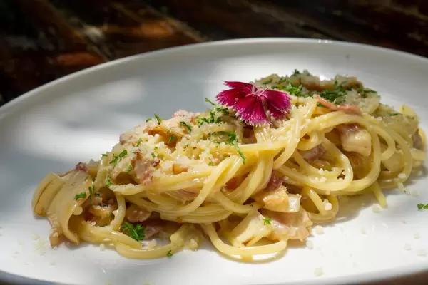 Spaghetti Carbonara mit Speck, Geriebenen Parmesan Käse, Pilzen, Zwiebeln und Kräutern auf einem weißen Teller in der Sonne Nahaufnahme