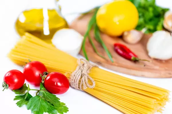 Spaghetti mit Gemüse und Gewürzen, Olivenöl und Chili vor Holzbrett