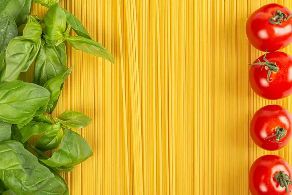 Spaghetti with basil leaves and cherry tomatoes, top view