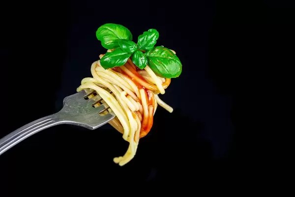 Spaghetti with tomato sauce and basil leaves on a fork, close-up