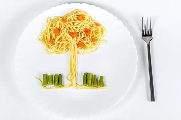 Spaghetti with vegetables in the shape of a tree. Lunch for a child on a white background, top view