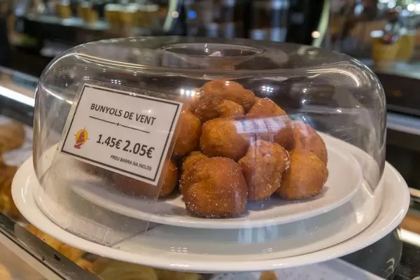Spanisches Krapfengebäck "Bunyols de vent" auf weißem Teller unter Tortenhaube in einem Café in Barcelona