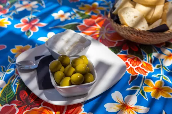 Spanish tapas: aioli dip and green olives served on a plate accompanied by bread on floral table cloth