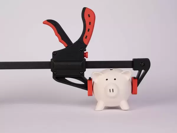 Sparschwein steckt in einer Klemme, vor weißem Hintergrund