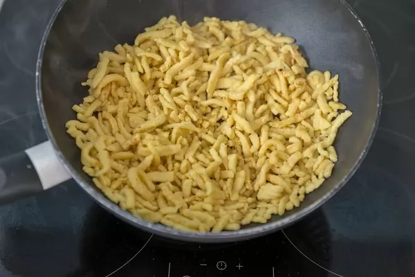 Spätzle in einem Wok werden für ein Gericht gebraten