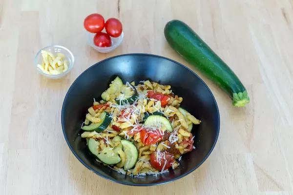 Spätzle mit getrockneten Tomaten und Zucchini mit Zutaten im Hintergrund