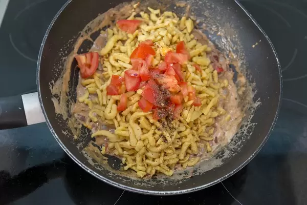 Spätzle noodles with cream sauce and tomatoes being prepared in a wok pan