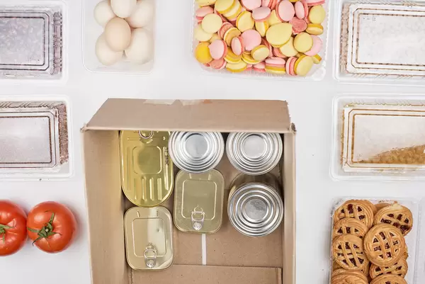 Spende für die Tafel: Blechdosen in einem Karton mit Tomaten, Eiern, Keksen und Trockenfrüchten