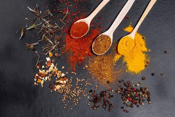 Spices in wooden spoons and scattered on a black background. Top view