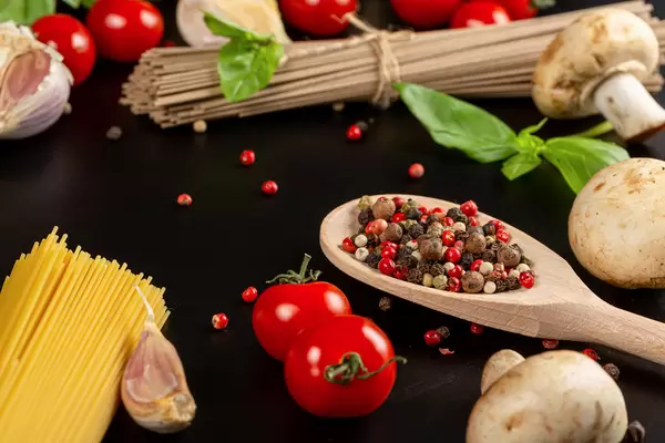 Spices, tomatoes, mushrooms and basil on a dark background with spaghetti
