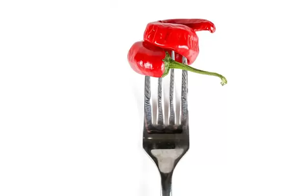 Spicy red chili peppers in the shape of a spiral on a white background with a fork