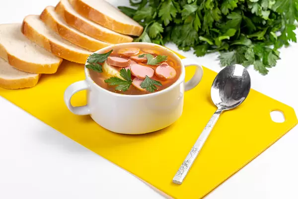 Spicy soup with carrots and sausages on the table with fresh parsley and slices of bread