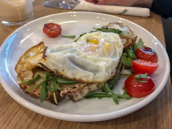 Spiegelei-Omelett auf knusprigem Toast mit Tomaten und Ruccola auf weißem Teller im Nahaufnahme