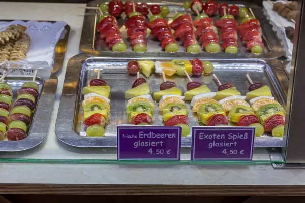 Spieße mit glasierten Früchten wie Erdbeeren, Trauben und tropischen Früchten wie Kiwis und Orangen