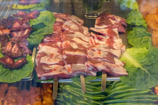 Spieße mit Schweinefleisch in einer Vitrine mit Salat und grünen Chilis