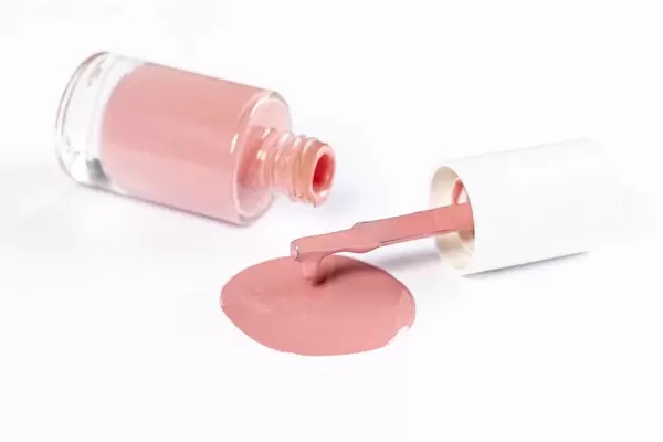 Spilled color nail polish with bottle and brush on white background