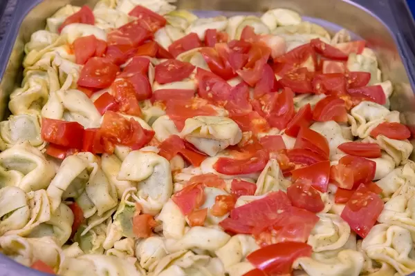 Spinach tortellini with tomatoes in cheese sauce, in a heat container at the buffet
