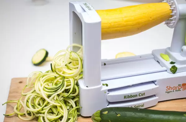 Spirulazer Küchengerät auf Holzbrett schneidet gelbe Zucchini in dünne Streifen mit grüner Zucchini im Vordergrund