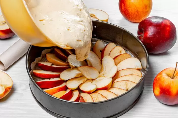 Sponge dough is poured into a baking sheet with apples. Apple pie recipe concept (Flip 2019)