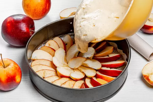 Sponge dough is poured into a baking sheet with apples. Apple pie recipe concept