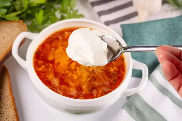 Spoon sour cream on a background of a bowl of tomato soup