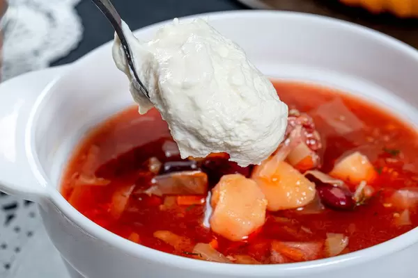 Spoon the sour cream put into a bowl of borscht close up