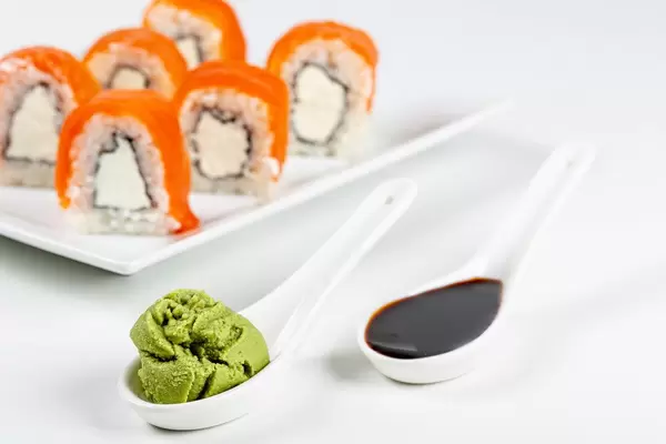 Spoons with soy sauce and wasabi on white, Philadelphia sushi behind