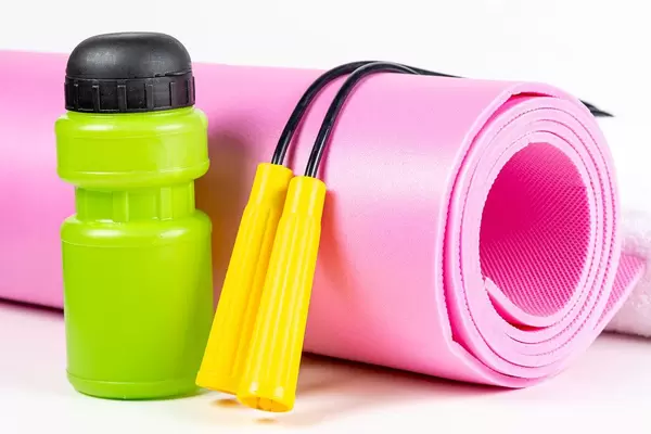 Sport lifestyle concept - yoga mat, jump rope and water bottle on white background