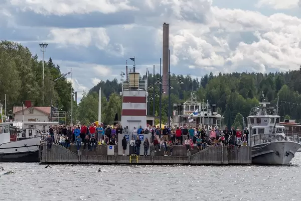 Sportbegeisterte Zuschauer stehen und sitzen beim Leuchtturm am Hafen von Lahti, Finnland & blicken auf Ironman-Teilnehmern beim Schwimmwettkampf