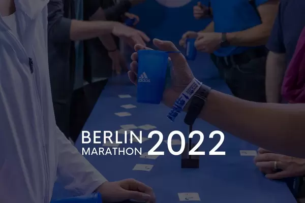 Sportler am Adidas-Stand mit Getränkebechern und dem Bildtitel "Berlin Marathon 2022"