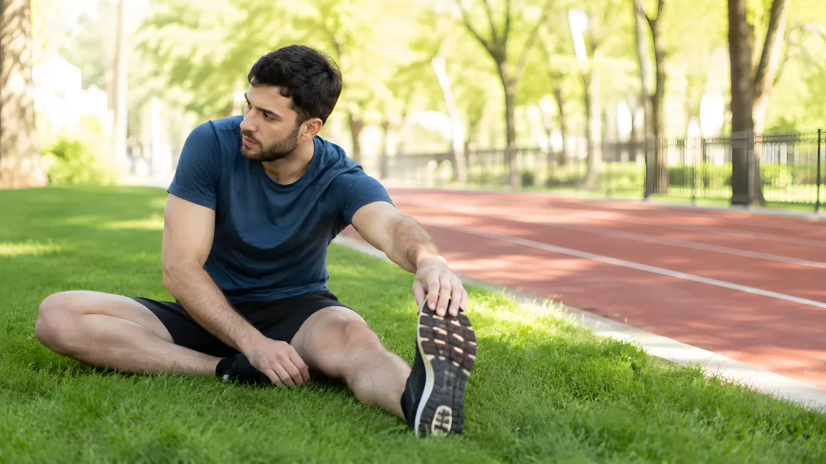 Sportler dehnt sich auf Rasen neben Laufbahn