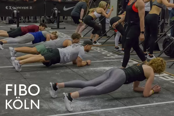 Sportler nehmen an der Plank Challenge teil und machen gemeinsam Fitness, neben dem Bildtitel Fibo Köln