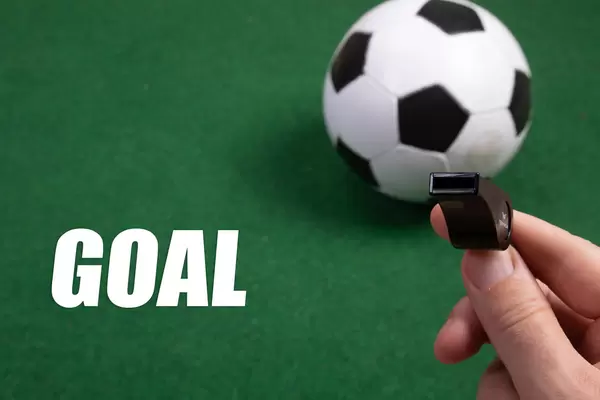 Sports whistle, soccer ball and Goal text on green grass