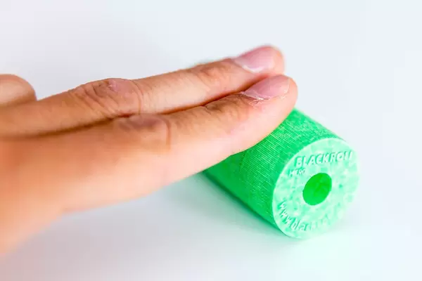 Sportsman puts two finger on the Blackroll's green fascia roll, on a white surface, to release tensions and to strengthen his hand muscles