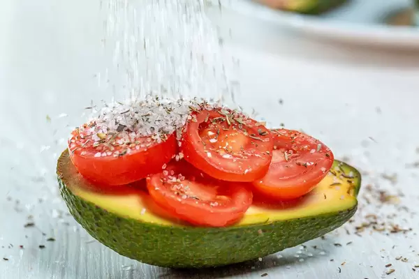 Sprinkle salt and spices on avocado stuffed with tomatoes