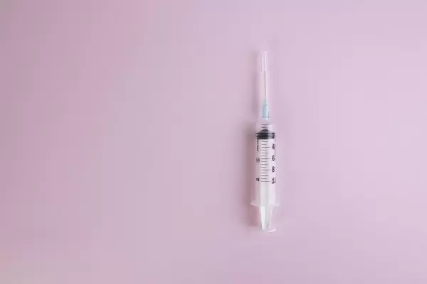 Spritze mit Flüssigkeit auf rosa Hintergrund