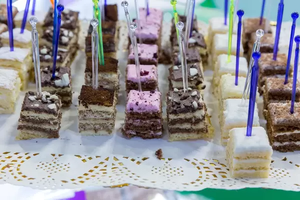 Square pieces of different cakes displayed in rows and served with multicoloured plastic cake picks