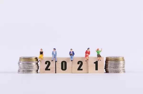 Stack of coins and group of people sitting on wooden cubes with 2021 text