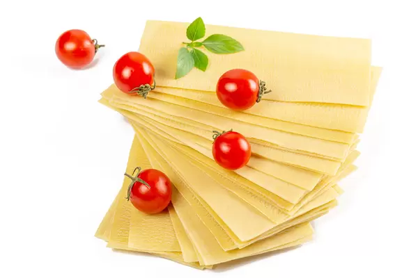Stack of dried lasagna sheets with cherry tomatoes and basil
