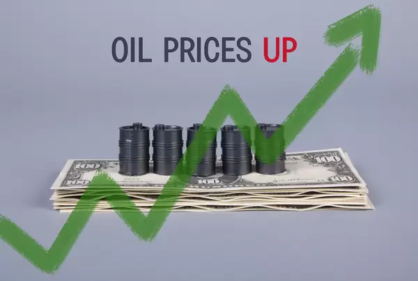 Stack of money and oil barrels with green up chart and Oil Prices Up text