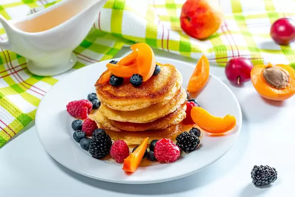 Stack of pancakes with fruit blueberries, raspberries, mulberry, apricot pieces and honey (Flip 2019)