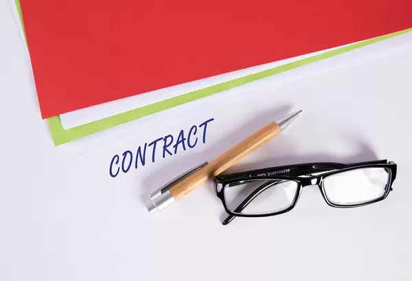 Stack of papers with pen, glasses and Contract text