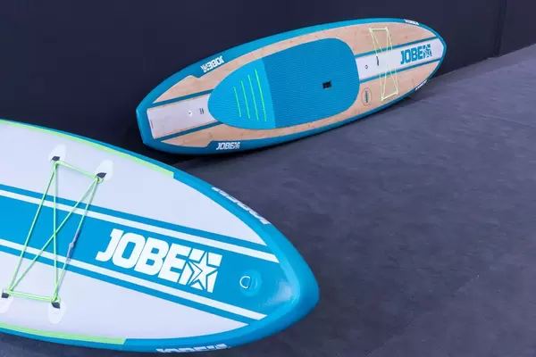 Stand up Paddle Boards (SUP), eines aufblasbar und eines aus Bambus vor grauem Hintergrund