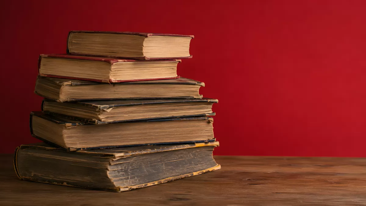 Stapel alter Bücher auf Holztisch vor roter Wand