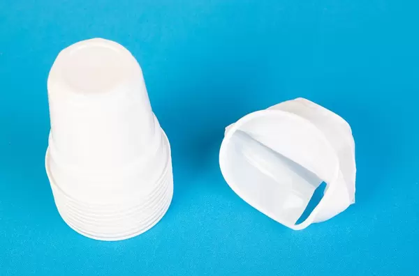 Stapel Plastikbecher und zerknüllter umweltschädlicher Einwegbecher vor blauem Hintergrund