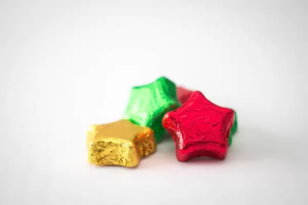 sternförmige Weihnachtsschokolade in gelber, roter und grüner Aluminiumverpackung vor weißem Hintergrund
