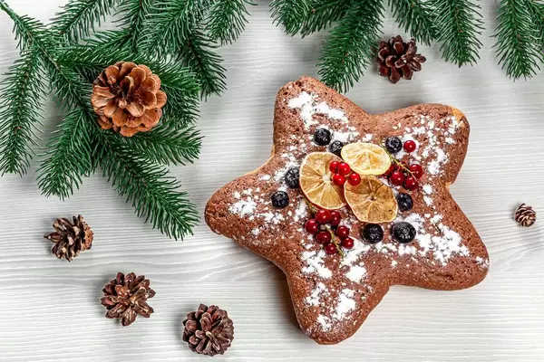 Sternförmiger Biskuitkuchen mit roten Johannisbeeren, Heidelbeeren und getrockneten Zitrusfrüchten, Aufnahme von oben mit Weihnachtsdeko