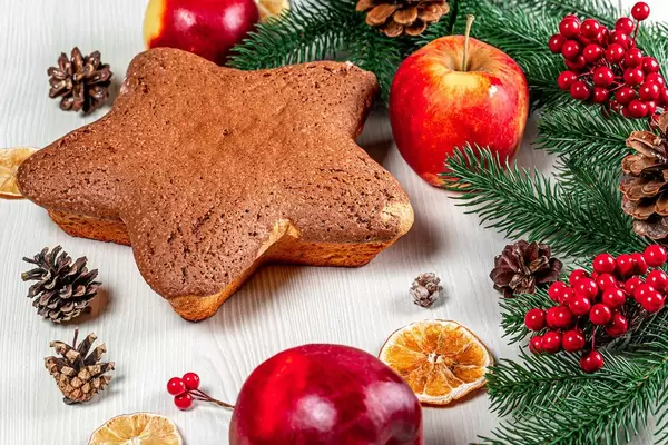 Sternförmiger Kuchen auf dem Tisch mit Äpfeln, getrockneten Zitrusfrüchten und Weihnachtsdeko